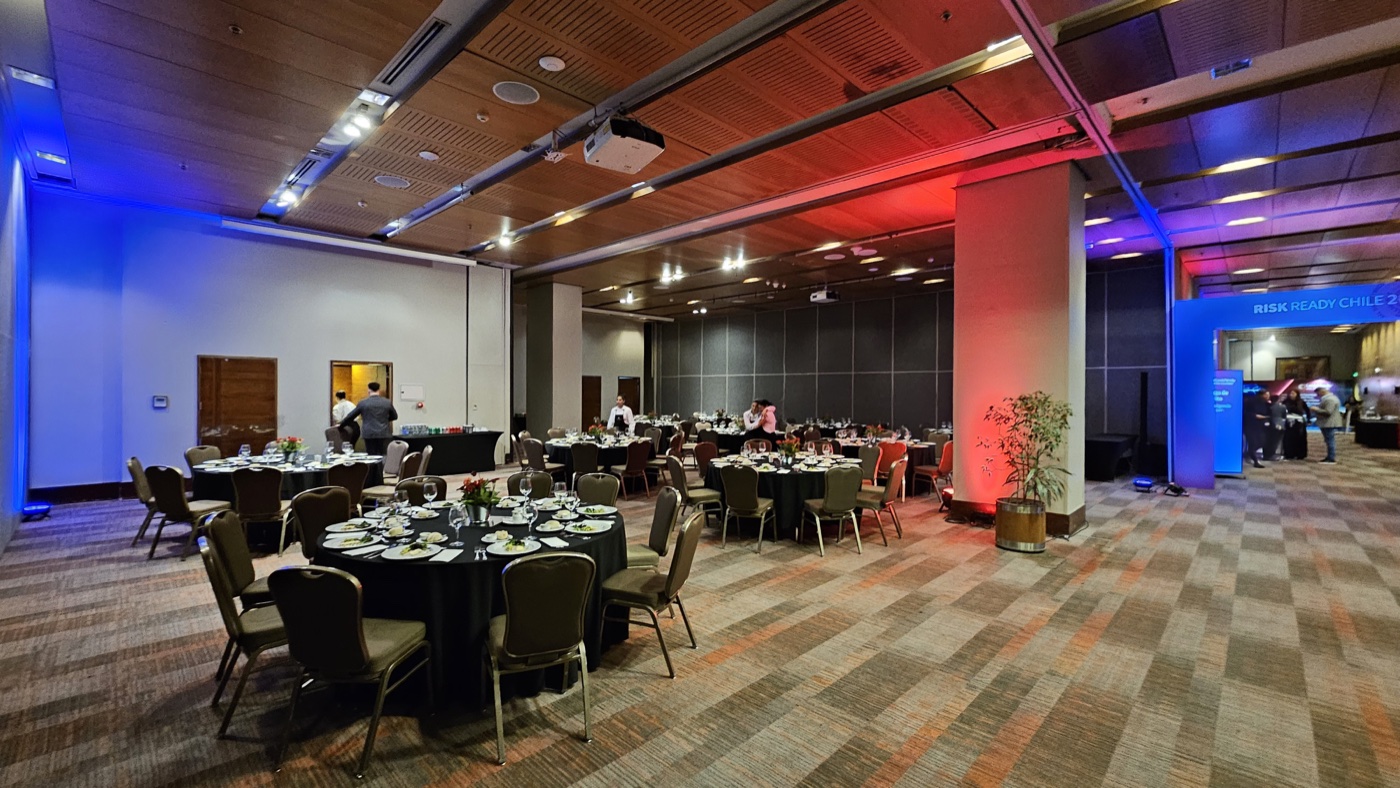Salón preparado con mesas, iluminación azul y roja y acceso de RiskReady Chile 2025